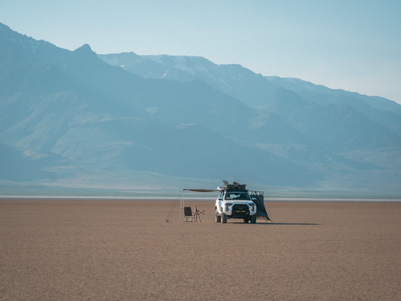 Dispersed camp with an awning on a dry lakebed, mountains in the distance