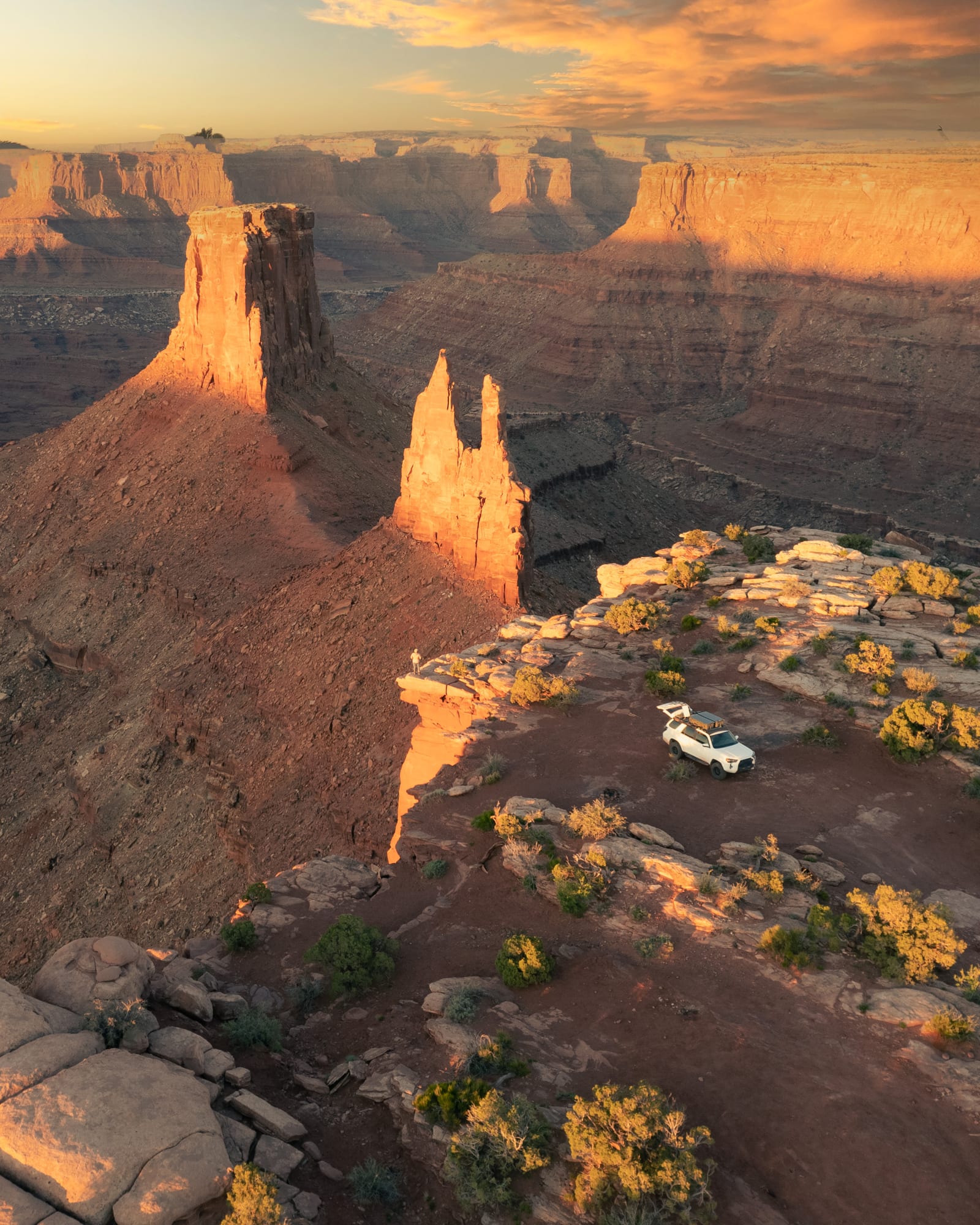 Truck parked at a canyon-rim overlook at golden hour, sandstone towers lit by low sun