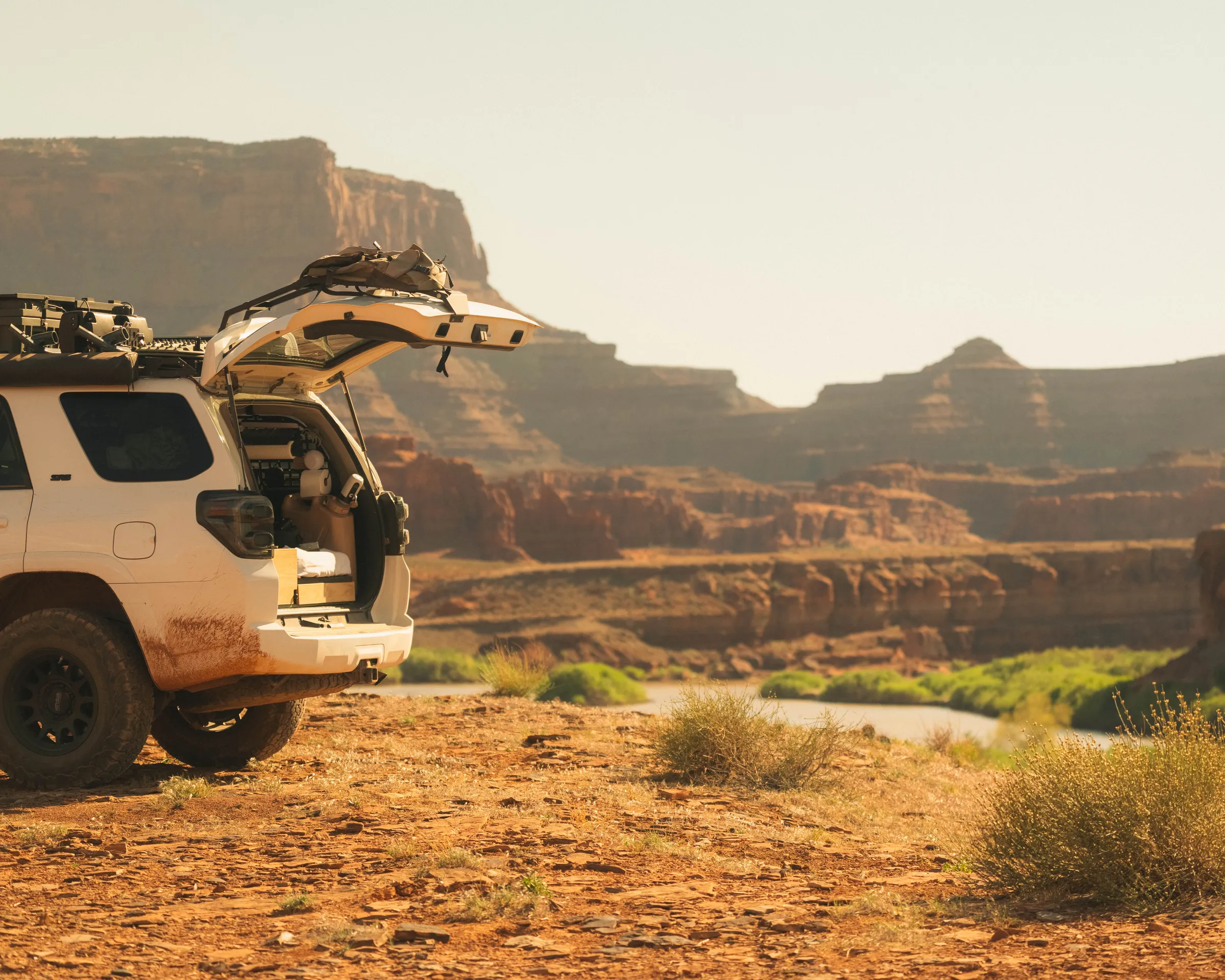 A muddy overland 4Runner with its hatch open, parked at a canyon overlook above a river in Utah